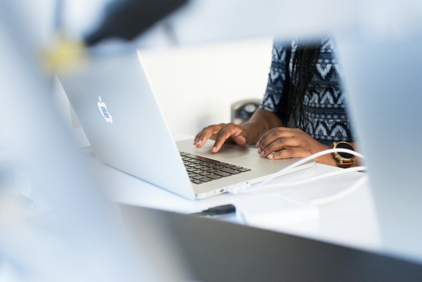 Woman typing on a silver laptop at a white desk.