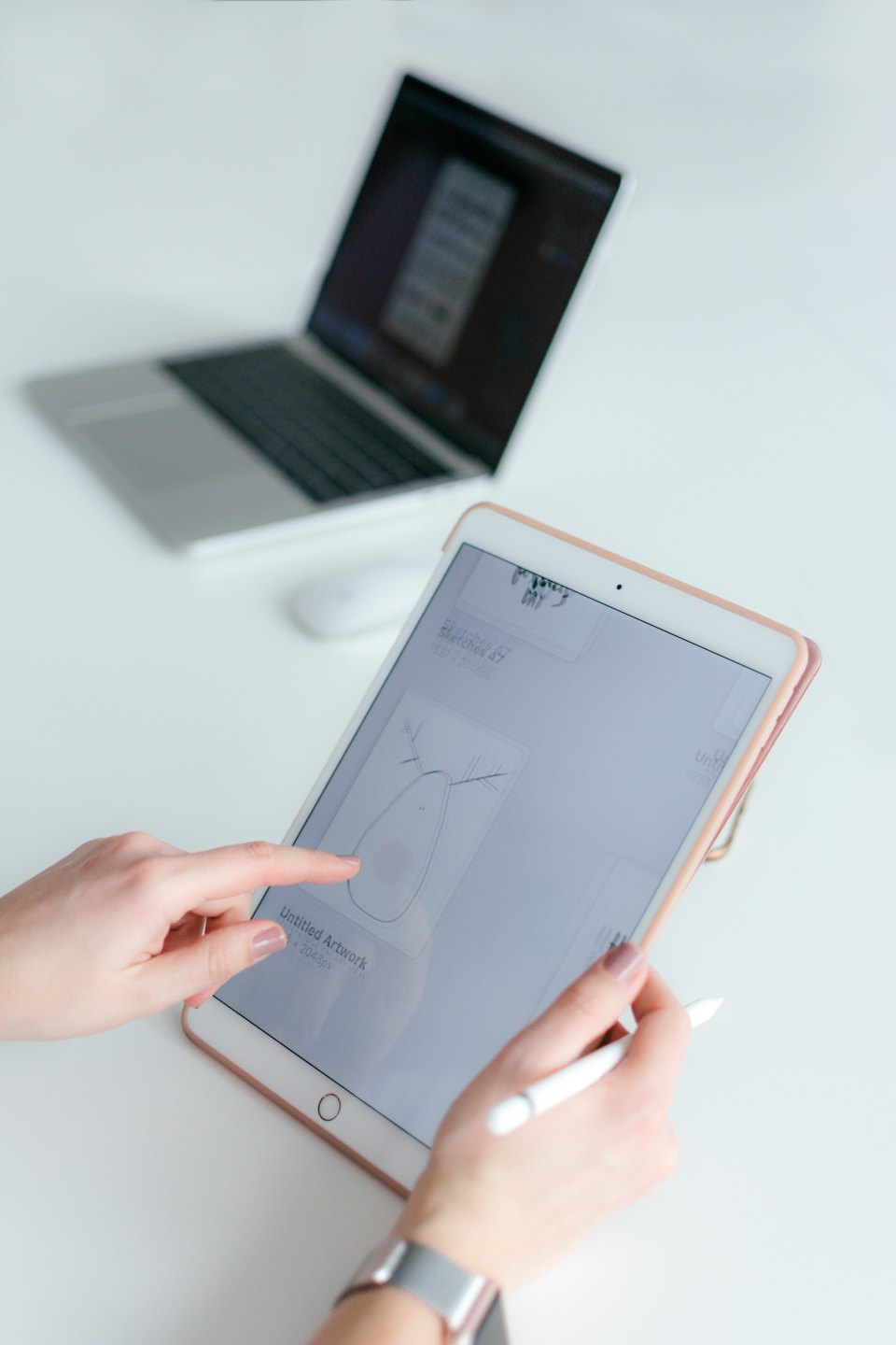Hands using a tablet and stylus on a white desk.